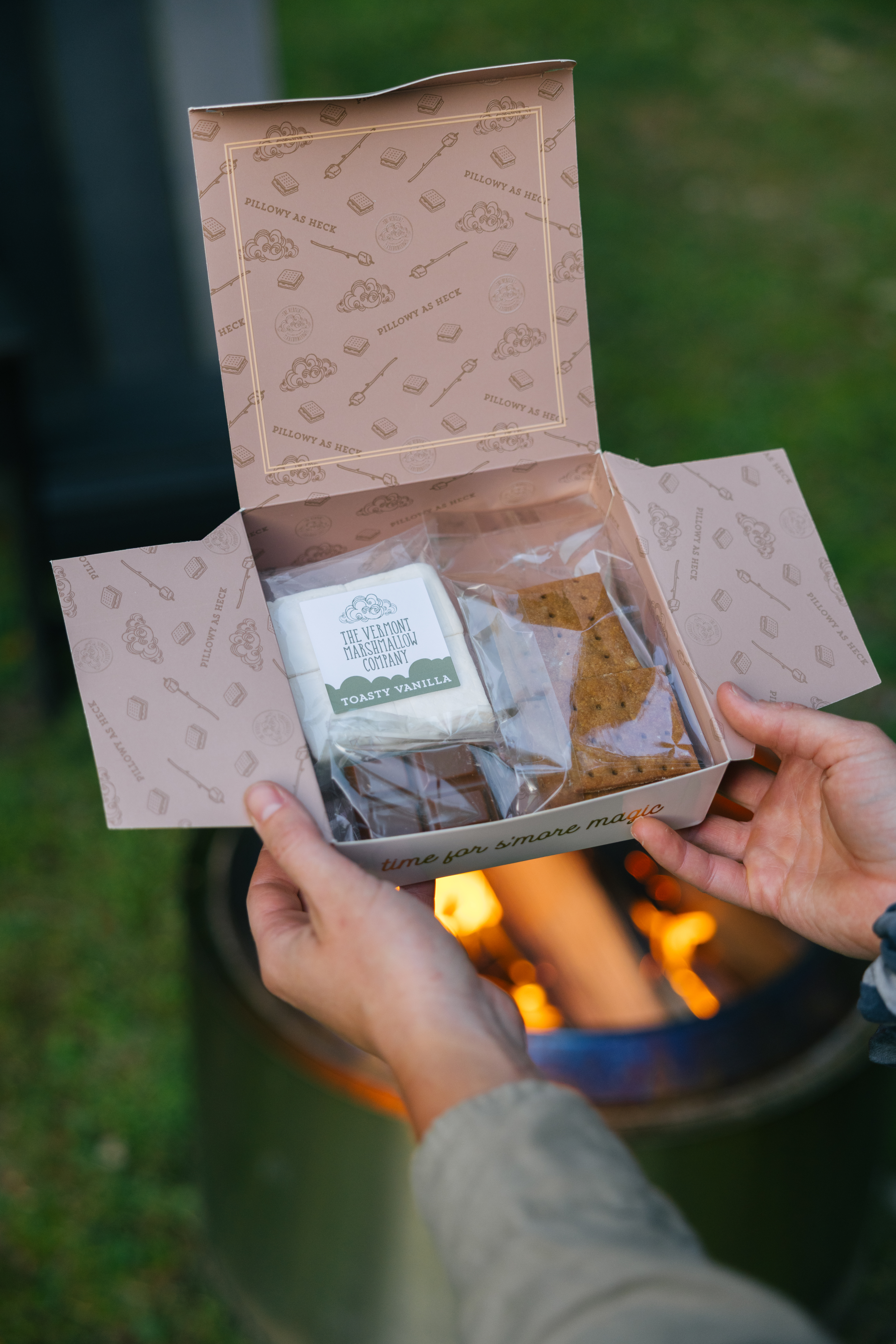 Hands holding a welcome gift box with snacks near an outdoor fire